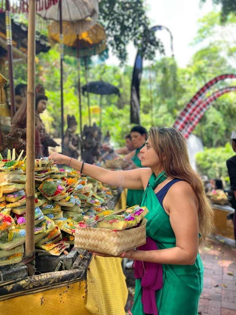 Woman in a green wrap placing flower offerings at a Balinese temple