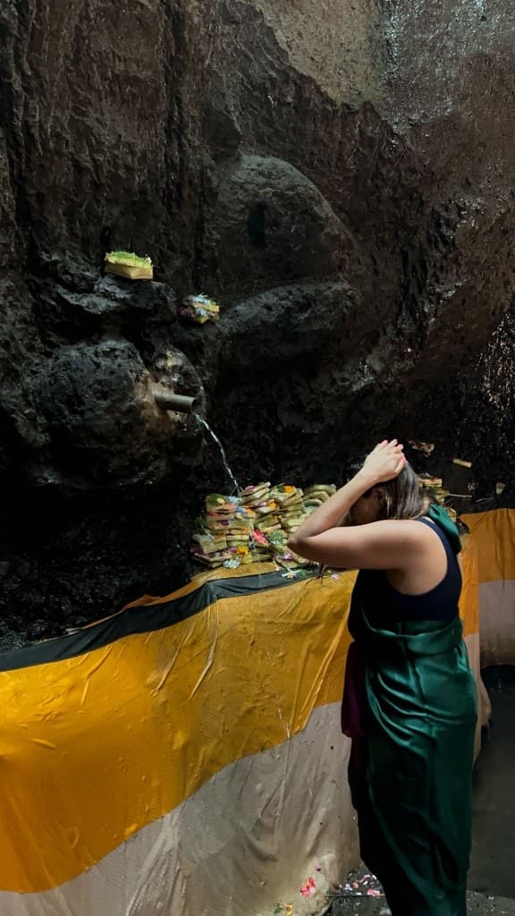 Woman at a sacred water spout with Balinese flower offerings in a cave shrine