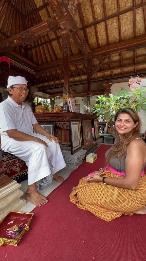 Woman in a traditional sarong seated with a Balinese elder in a carved wooden pavilion