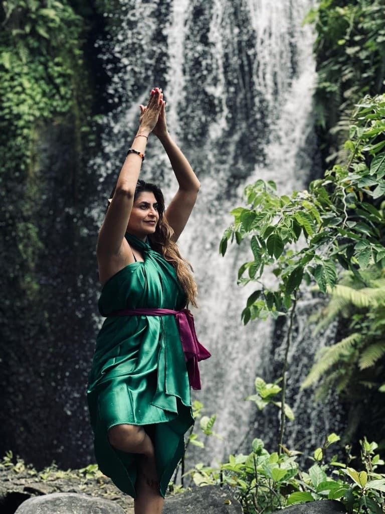 Woman in a green dress practicing a standing yoga pose before a tropical waterfall