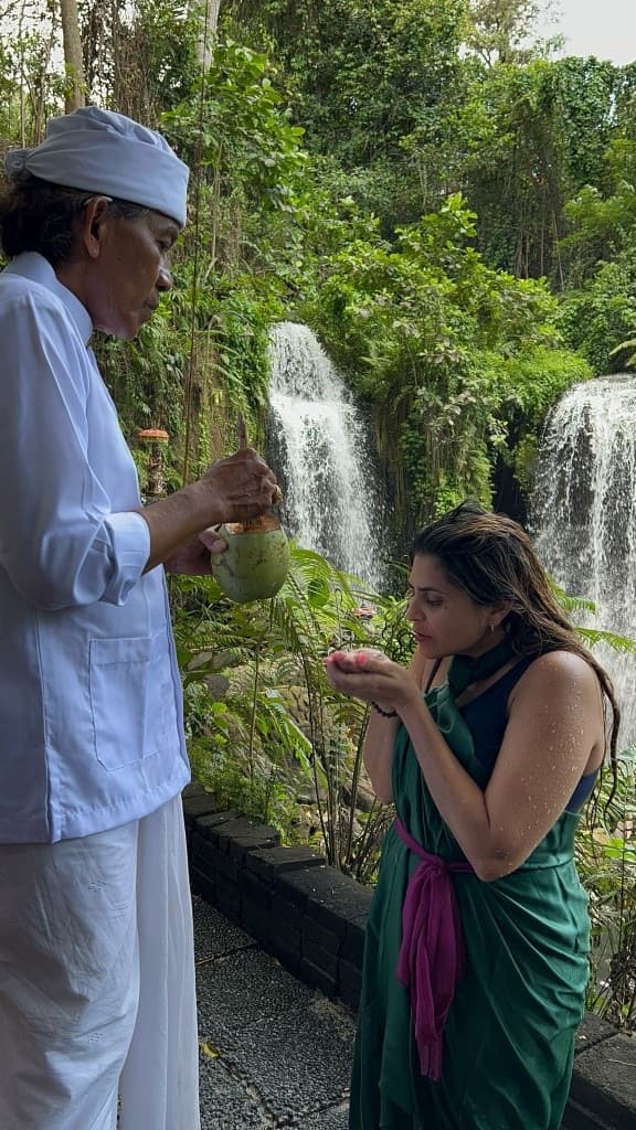 Woman receiving a traditional water blessing near tropical waterfalls in Bali