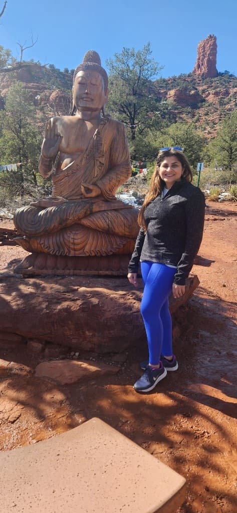 Woman standing beside a Buddha statue with Sedona red rocks behind