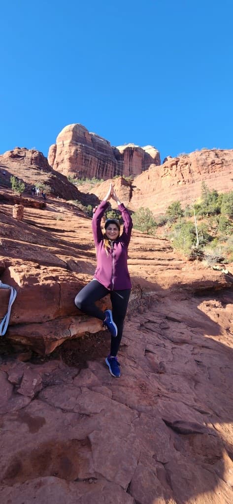 Woman in a purple jacket practicing a standing yoga pose on Sedona red rocks
