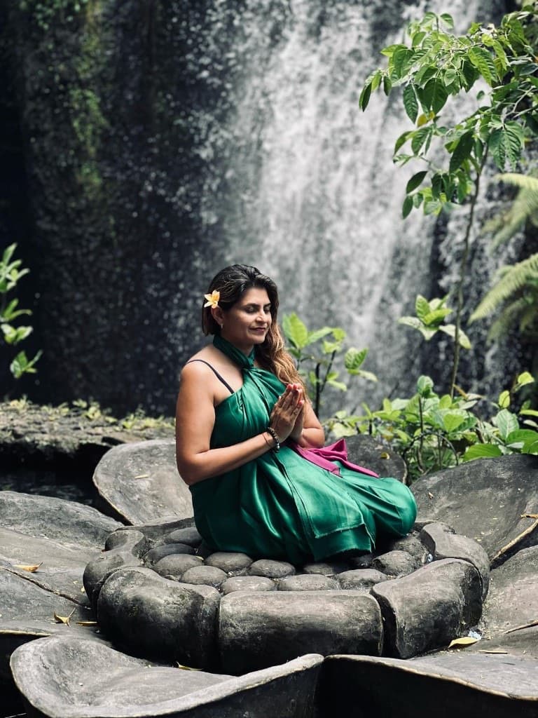 Woman seated in meditation on a stone lotus pedestal before a tropical waterfall